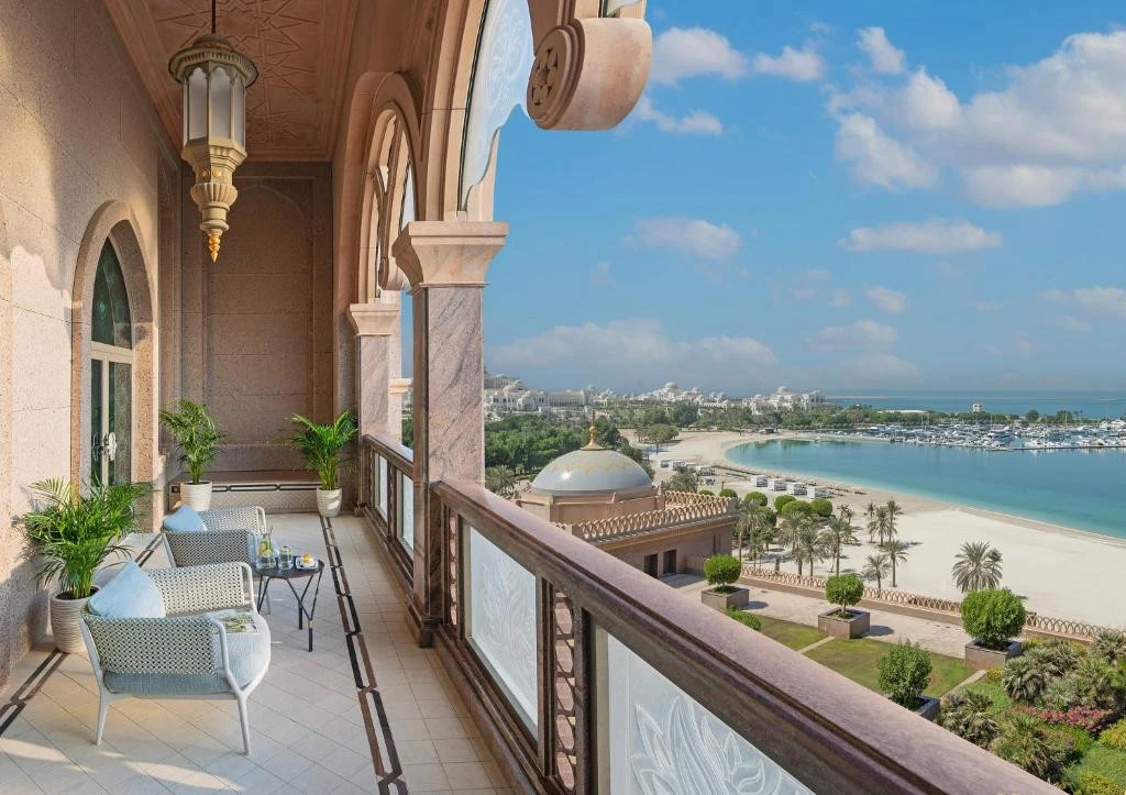 Emirates Palace balcony overlooking beach and gardens, Abu Dhabi skyline visible.