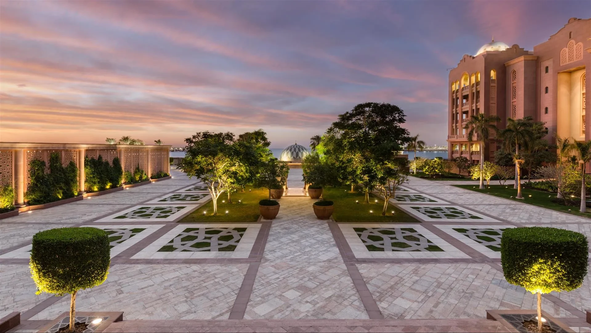 Emirates Palace gardens at sunset, Abu Dhabi, with ornate architecture.