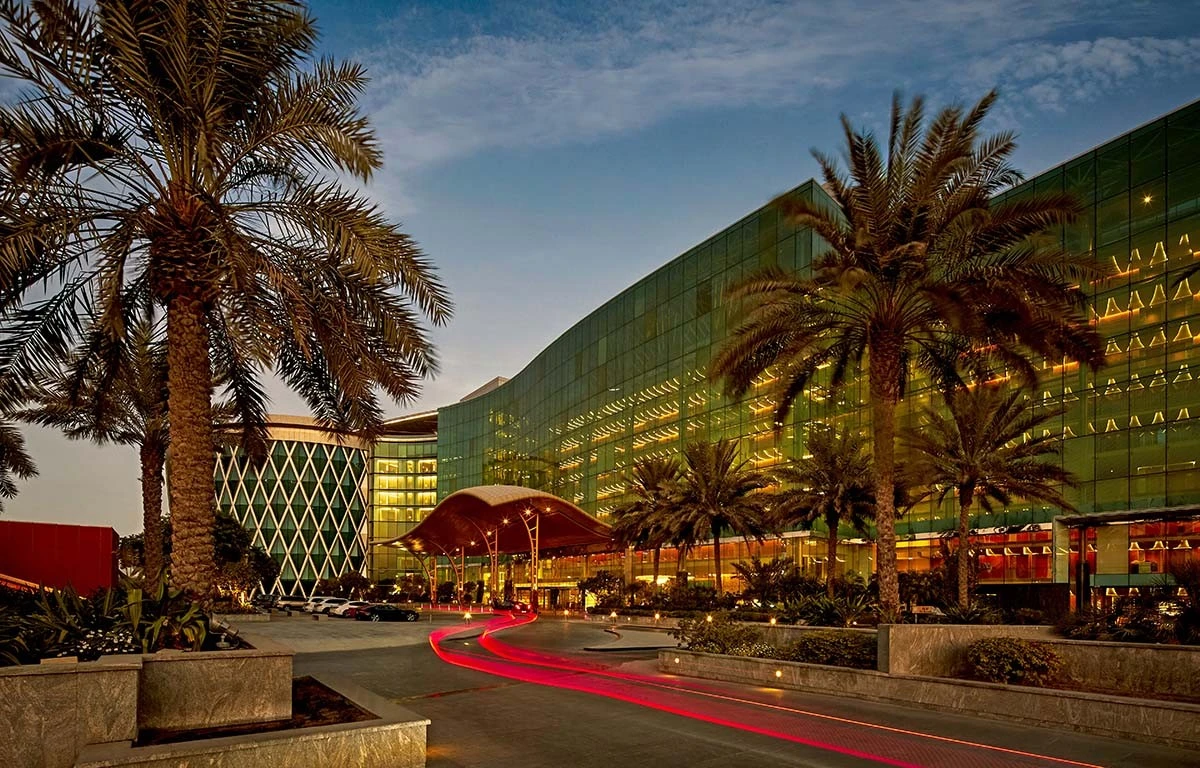 The Meydan Hotel exterior with palm trees, Dubai at dusk.