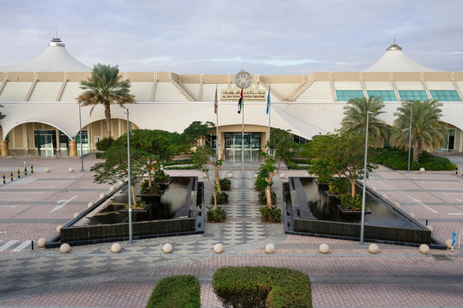 ADNEC Centre Al Ain entrance with palm trees and fountains.