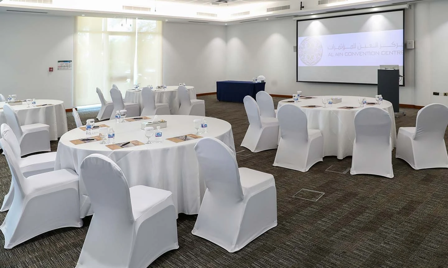 ADNEC Centre Al Ain conference room with round tables and chairs.